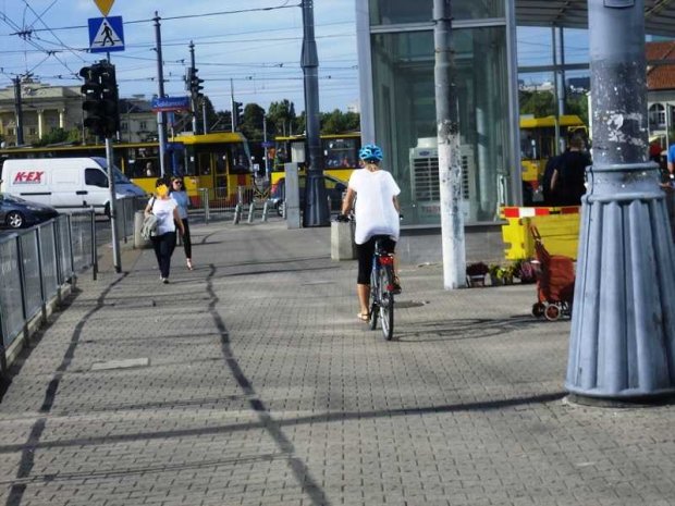 Rowerzystka na chodniuku przy wejściu do stacji Metro Ratusz-Arsenał