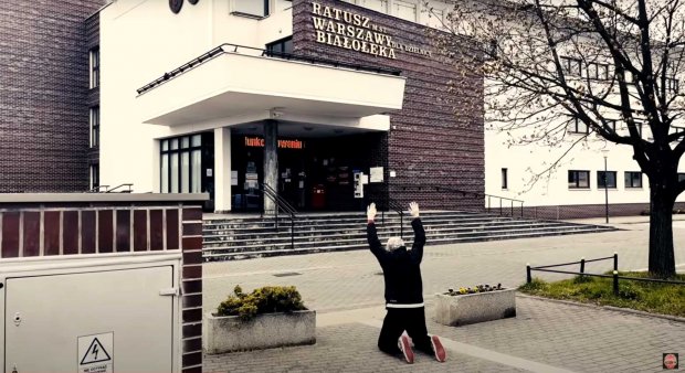 Kazik klęczy przed urzędem w Białołęce kadr z teledysku zespołu KULT