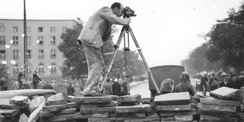 Amerykański fotograf Julien Bryan filmuje podczas oblężenia Warszawy. Stoi on na szczycie barykady z kostki brukowej, które zostały wzniesione by zwolnić postęp armii niemieckiej