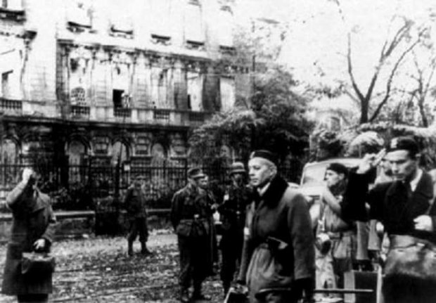 Tadeusz Komorowski Bór w cywilnym stroju, oddaje honory idącym do niewoli powstańcom. 5 październik 1944 r. Zdjęcie zrobione na ul. 6 sierpnia (obecnie Nowowiejskiej) na tle budynku Politechniki Warszawskiej.