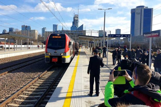 Widok na stację Warszawa Główna. Zawiadowca, podróżni stojący na peronie i pociąg stojący przy peronie. Fot. PLK